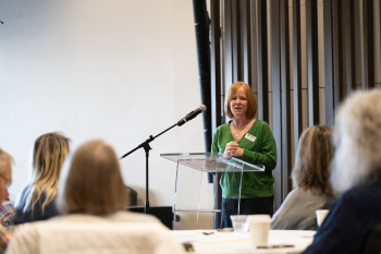 Woman speaking at a podium with guests watching