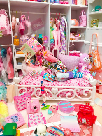 doll sitting on a bed reading a newspaper while in a room cluttered with many objects