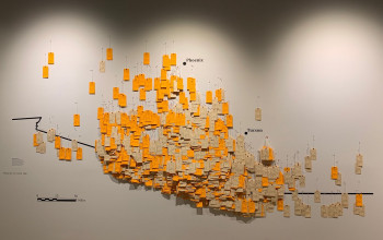 A wall covered with orange and beige tags with writing and cities in Arizona such as Tucson and Phoenix written on the wall with vinyl 