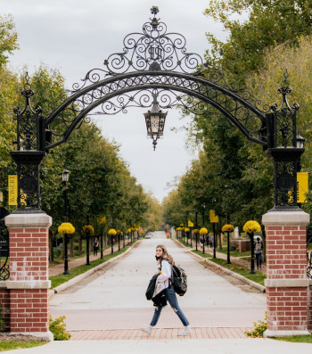 Female student walks under the arch on a fall day