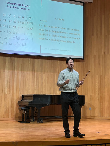 Man onstage with Chinese sheet music projected behind him