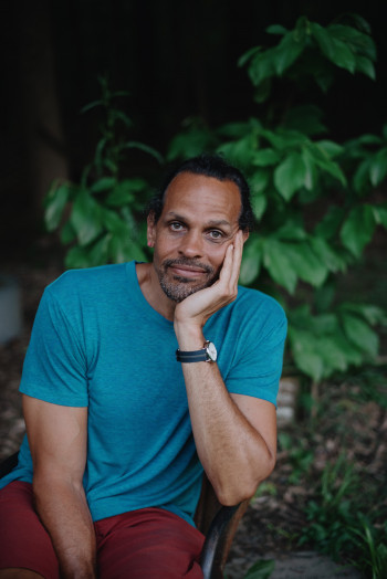 Ross Gay sitting with a wooded background