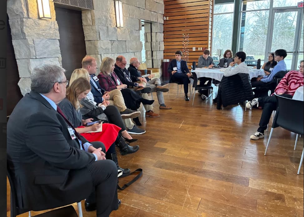 Students sit down board members (alumni), their communications coach (alumnus), faculty, and a reporter (Banner Graphic) to discuss crisis management strategy. 