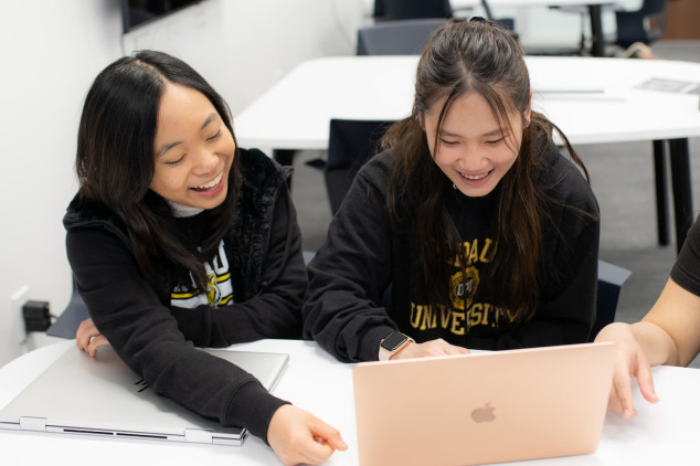 Three happy students working together on a laptop computer