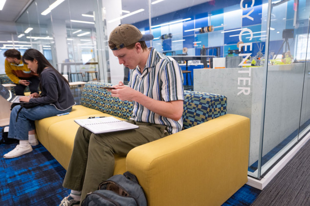 student looking at phone sitting on couch in front of technology center