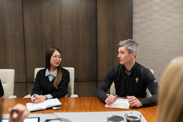 Student and alumni sitting at a table speaking during a meeting 