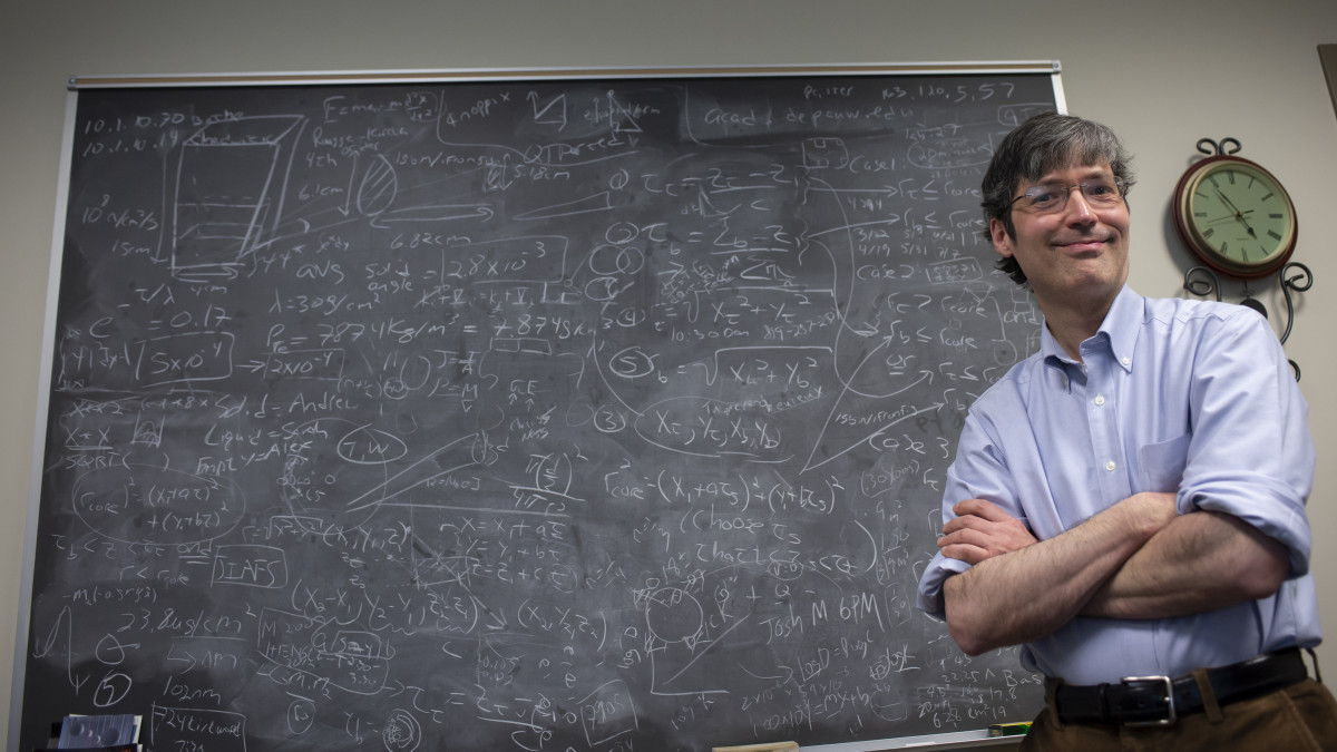 Alexander Komives poses in front of a chalkboard filled with information.