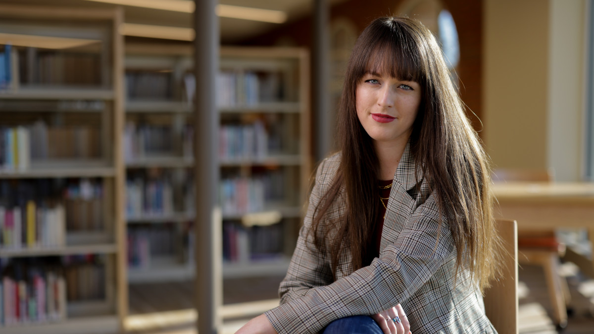 Brianna Scharfenberg sits in front of loaded bookshelves