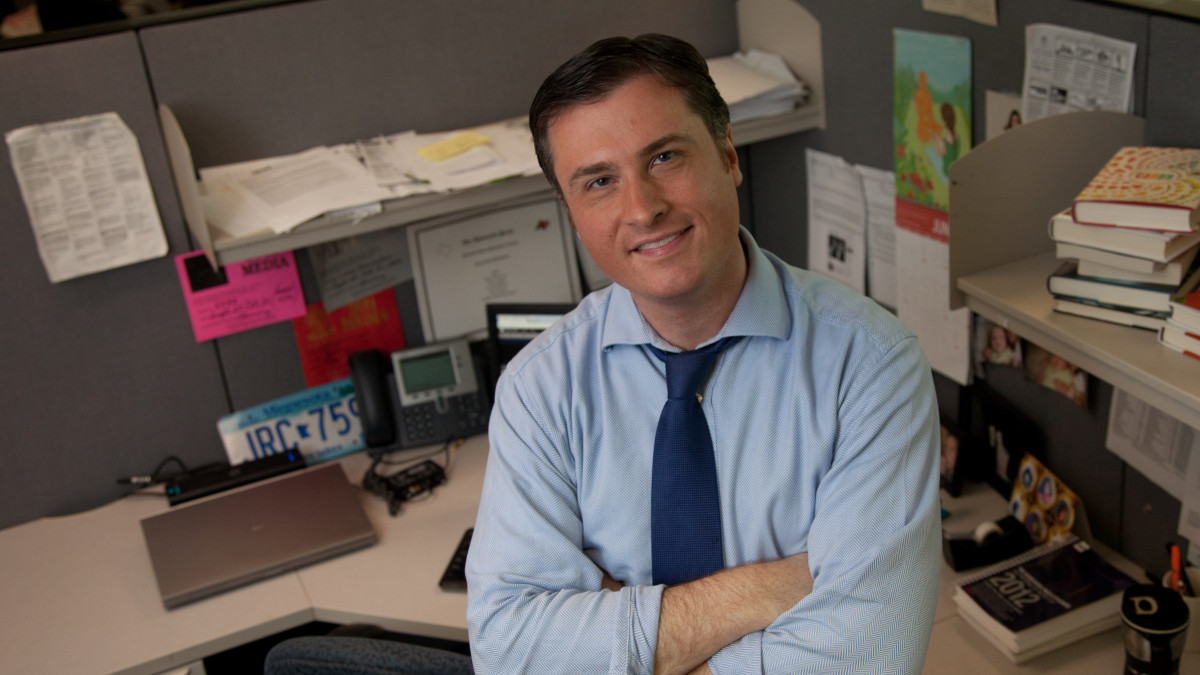 Eric Aasen '02 stands in the newsroom where he works