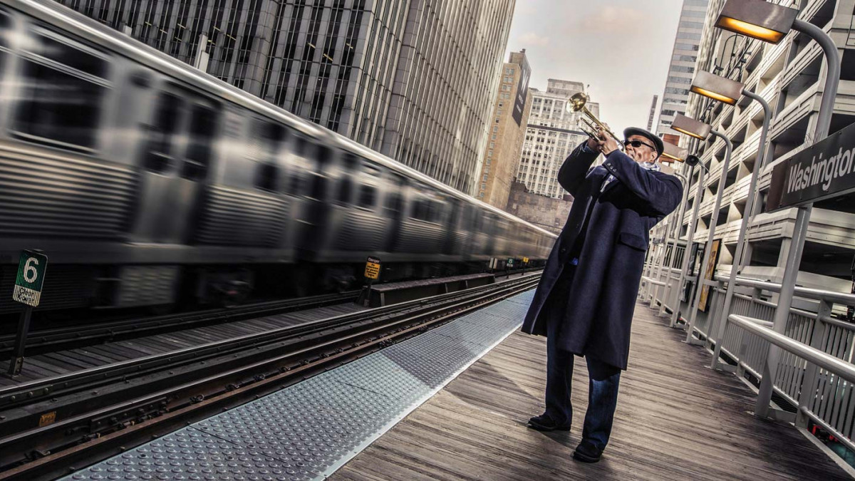 Pharez Whitted plays his trumpet beside a speeding subway train within a metropolitan scene