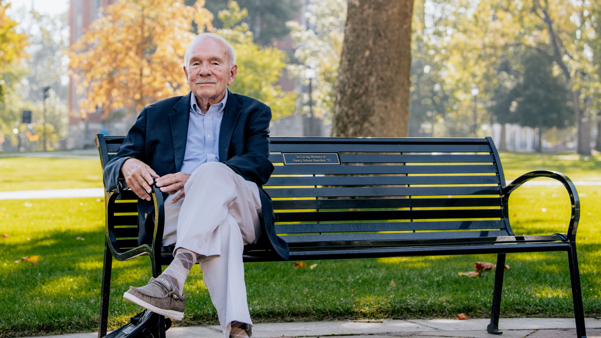 John Dittmer, professor emeritus, sits on a bench with East College in the background