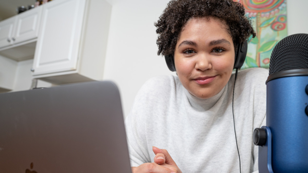 Lauren Clark sits at laptop computer and microphone for her podcast