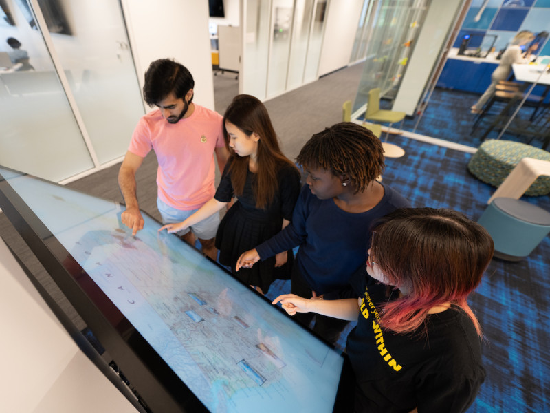 Four students collaborating on a large interactive digital screen
