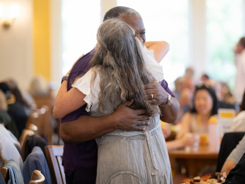 Two people sharing a warm embrace during a crowded indoor event.