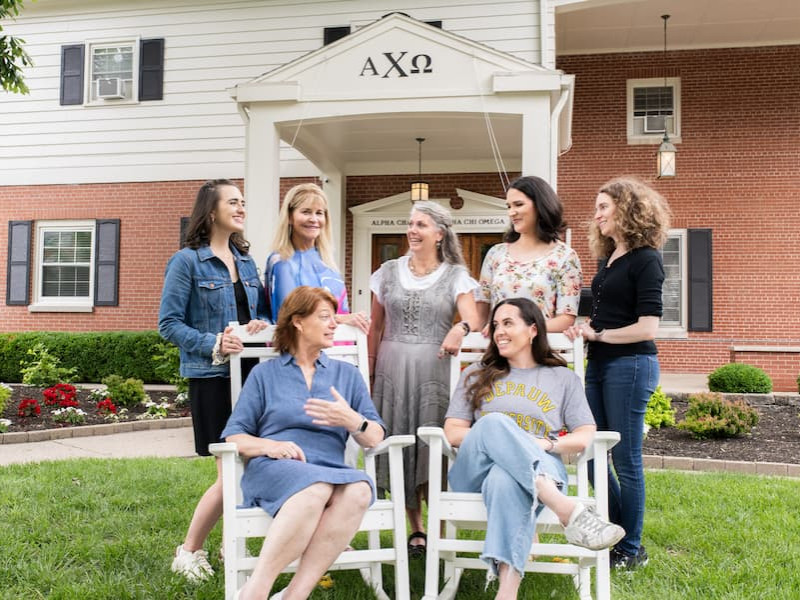 A multi-generational group of women posing in front of the Alpha Chi Omega sorority house.