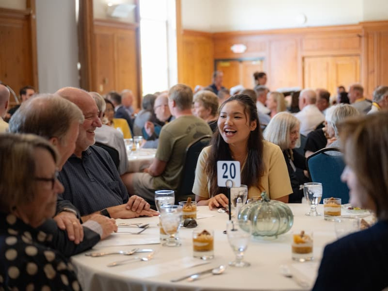 A young woman laughing while seated at a banquet table with guests during a formal lunch.