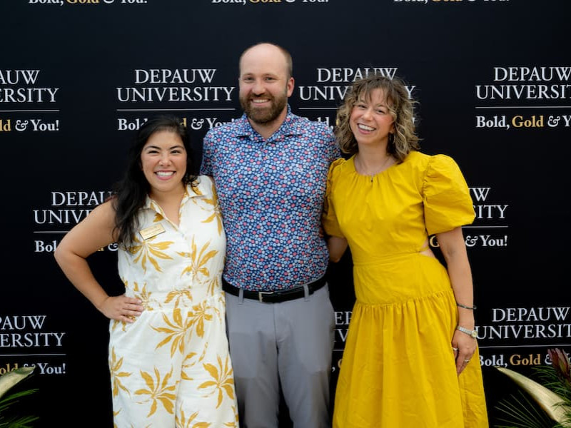 Three smiling alumni pose together in front of a black DePauw University Bold, Gold & You! backdrop.