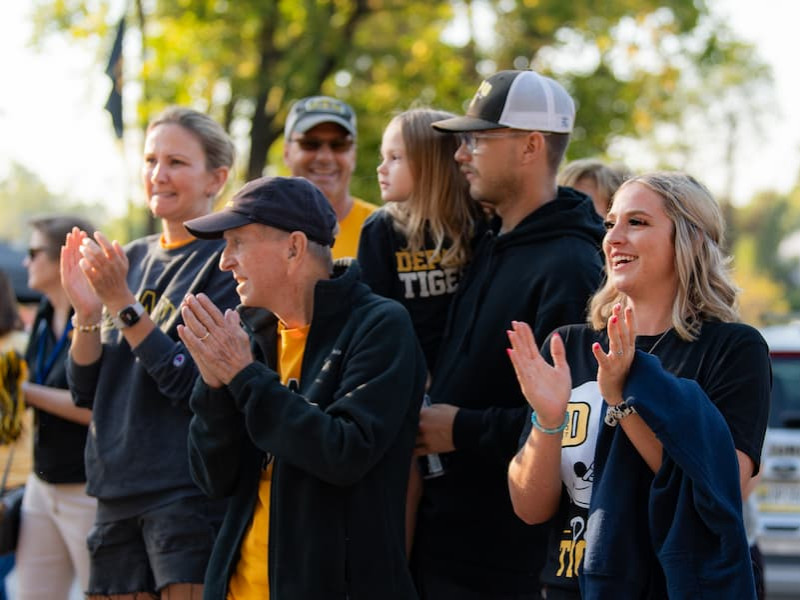 A diverse group of fans smiling and clapping at an outdoor sporting event.