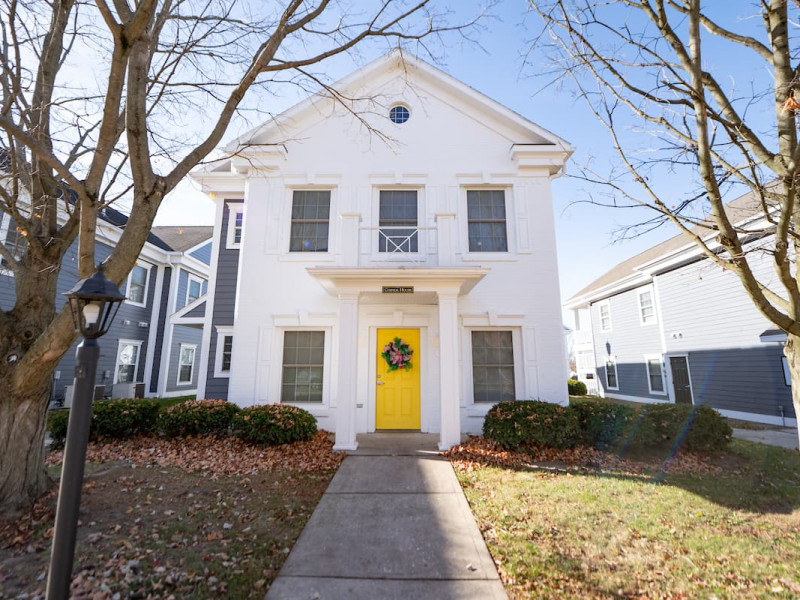 White duplex with yellow door, small balcony, and trees