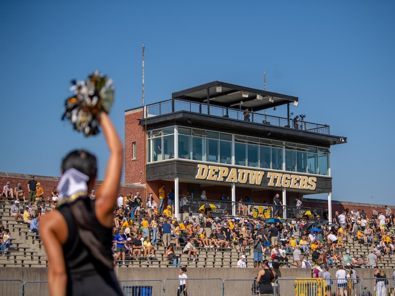 Cheerleader with pom-pom in front of press box and crowd