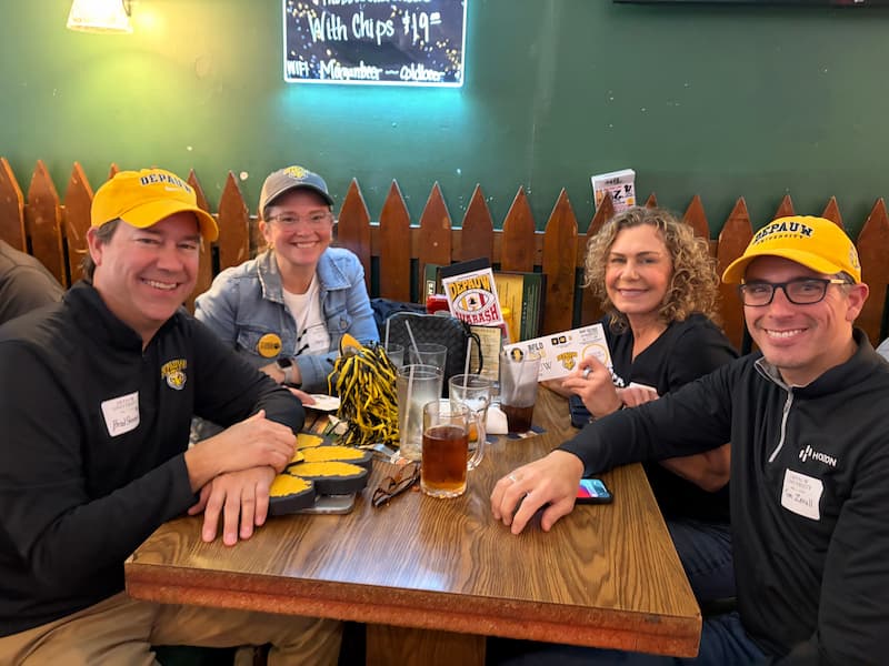 Four alumni in DePauw gear smiling at a table in a restaurant