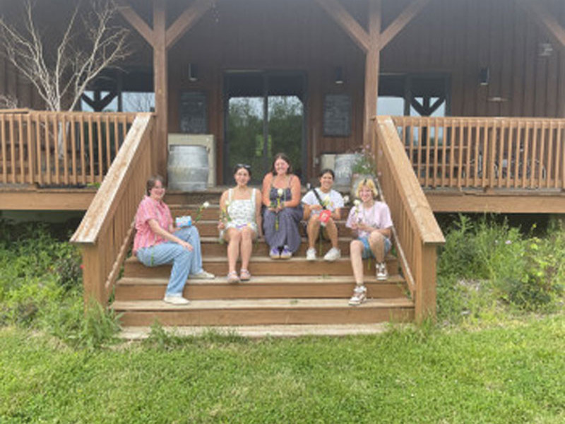 Five people sitting on wooden steps holding flowers