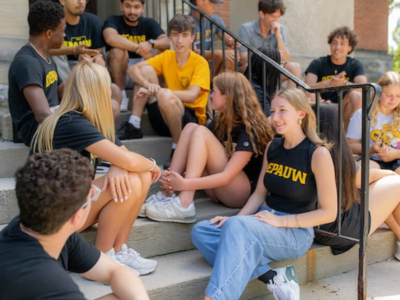 A group of DePauw University students sitting and talking together on a set of outdoor concrete stairs.