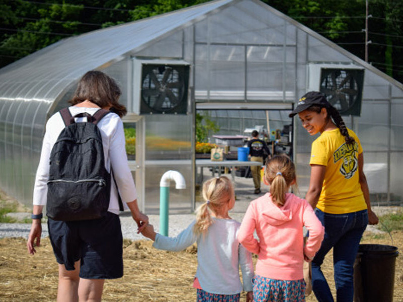 Adults and children walking toward a large greenhouse