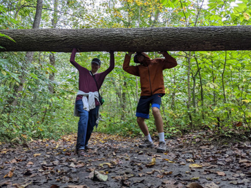 Two people posing under a fallen log on trail