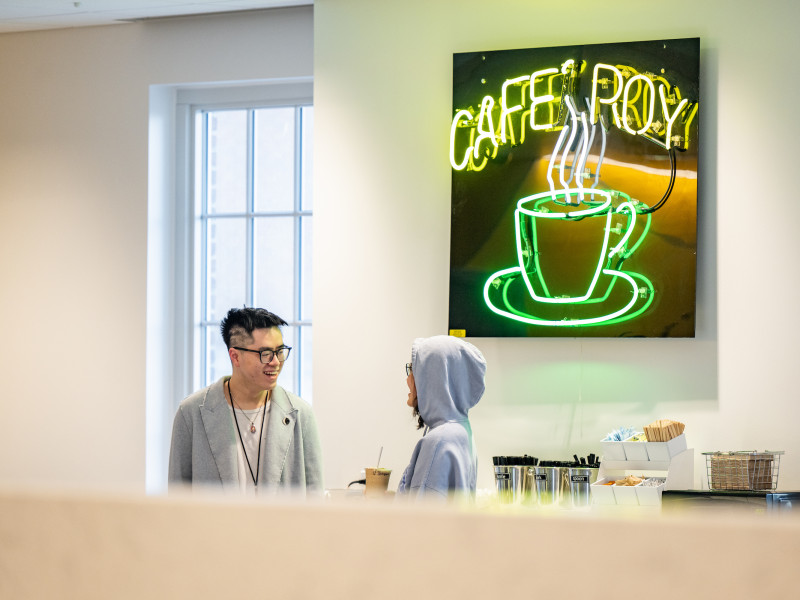 Two students talking beneath a neon Cafe Roy sign