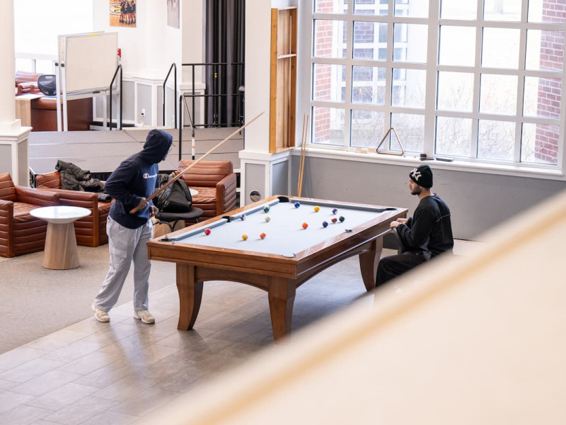 Two men playing pool in a spacious student lounge.