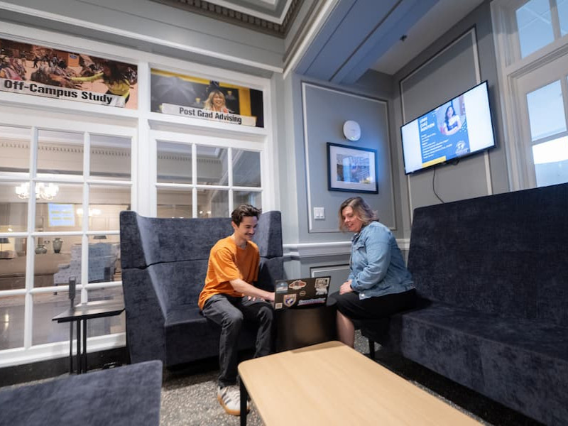 Two people discussing a laptop in a campus center lounge