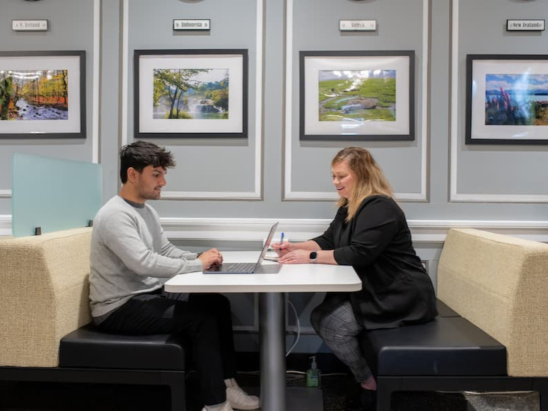 A student and advisor meeting at a booth with a laptop