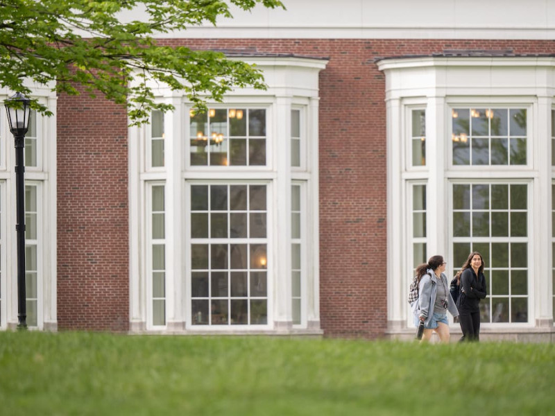 Two students walking past a brick campus building in spring.