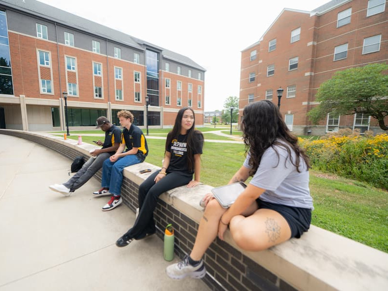 Four students sitting and talking on a campus quad