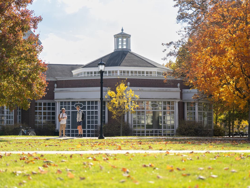 Two students talking outside a campus building during autumn.