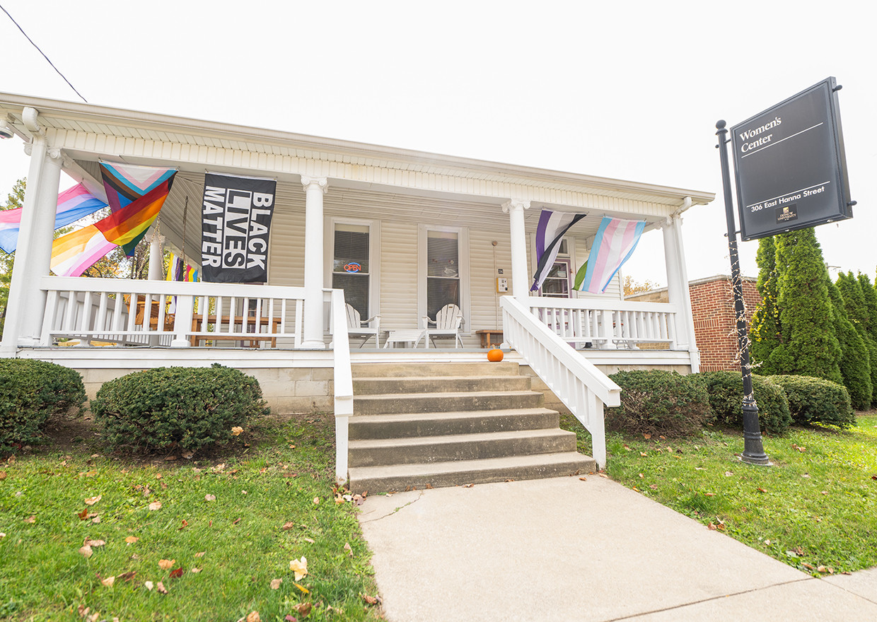 Exterior of the Women's Center, a white and brick building with BLM and LGBTQIA flags hanging on the patio.