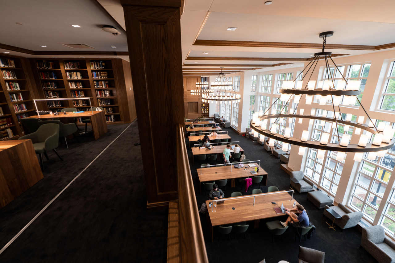 Split view of the Reading Room with bookcases and single-study areas to left (2nd floor) and communal study tables with a large wall of windows to right (1st floor).