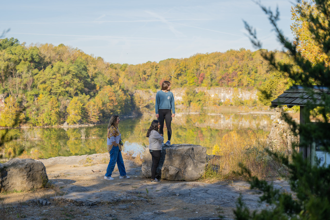 Three female students look out at the water and trees in the DePauw Nature Park in early Fall.
