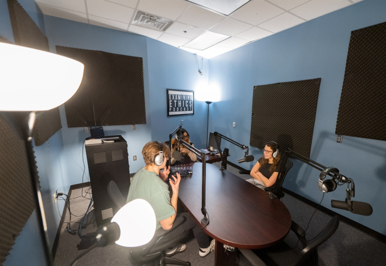 Two female students in over-ear headphones at a microphone recording a podcast